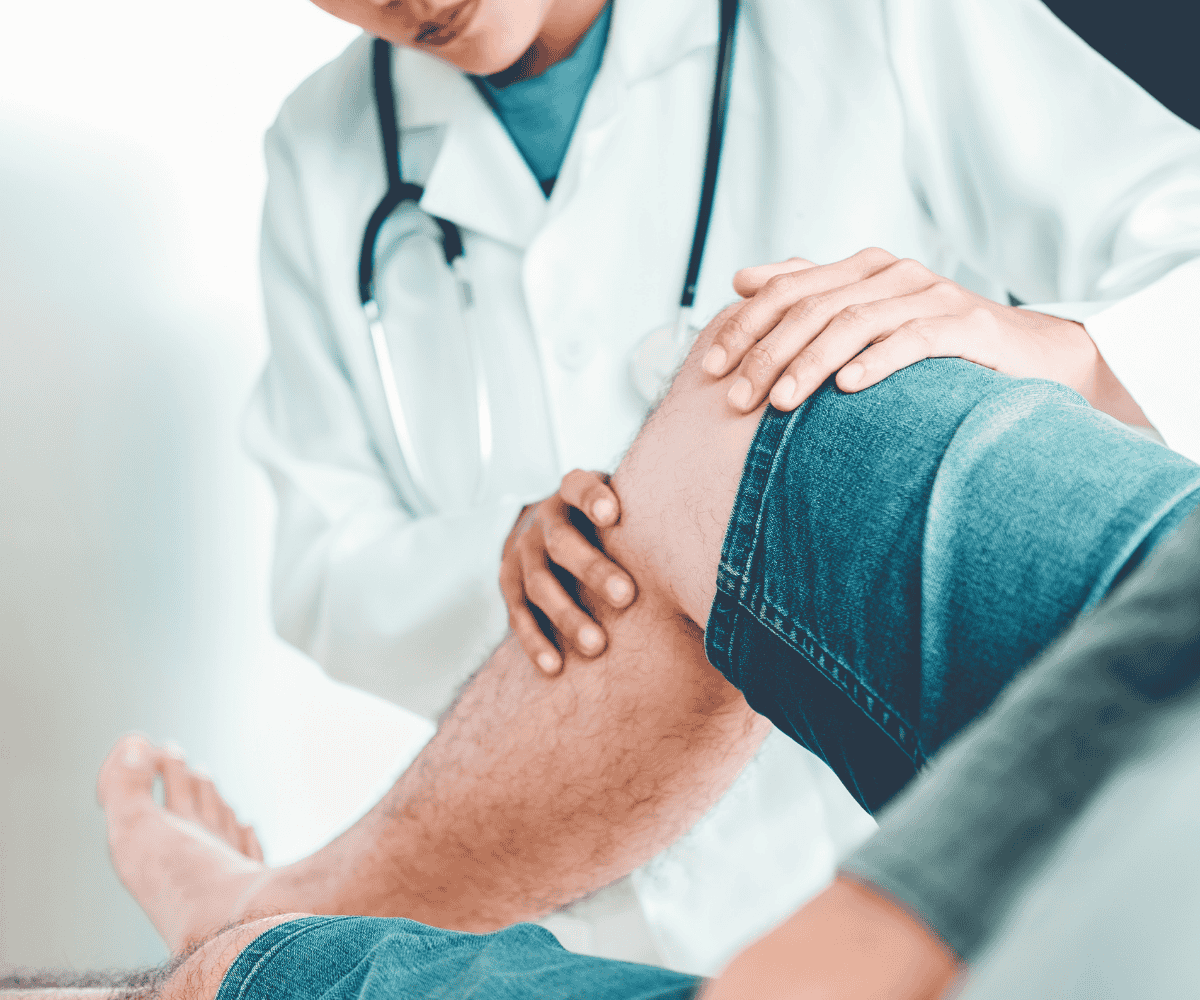 Clinician in a white coat examining a patients knee with both hands