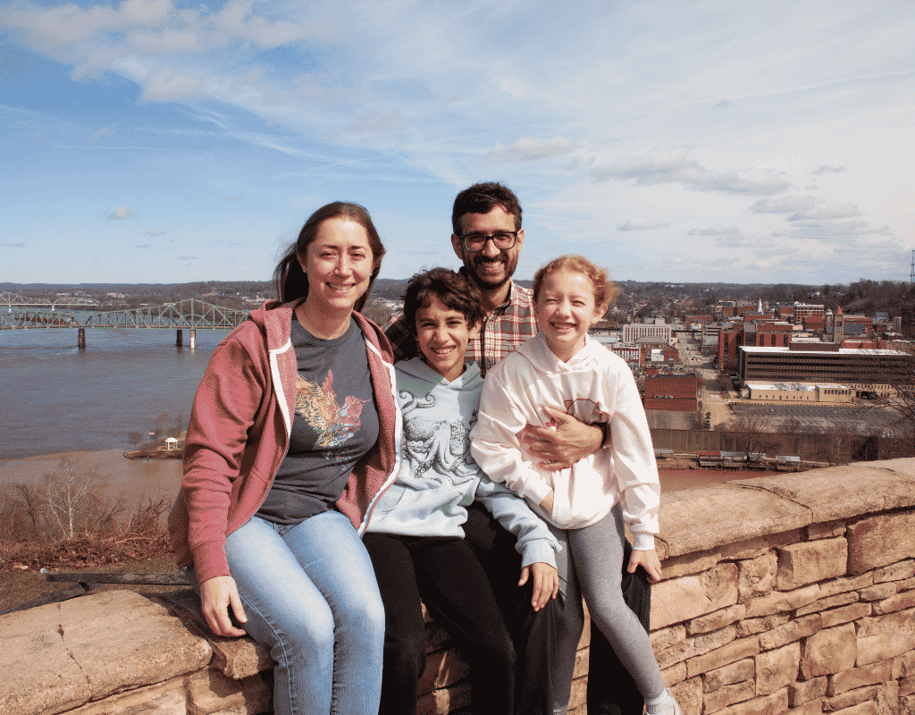 Family of four standing together on a hillside above a river town with a bridge in the distance