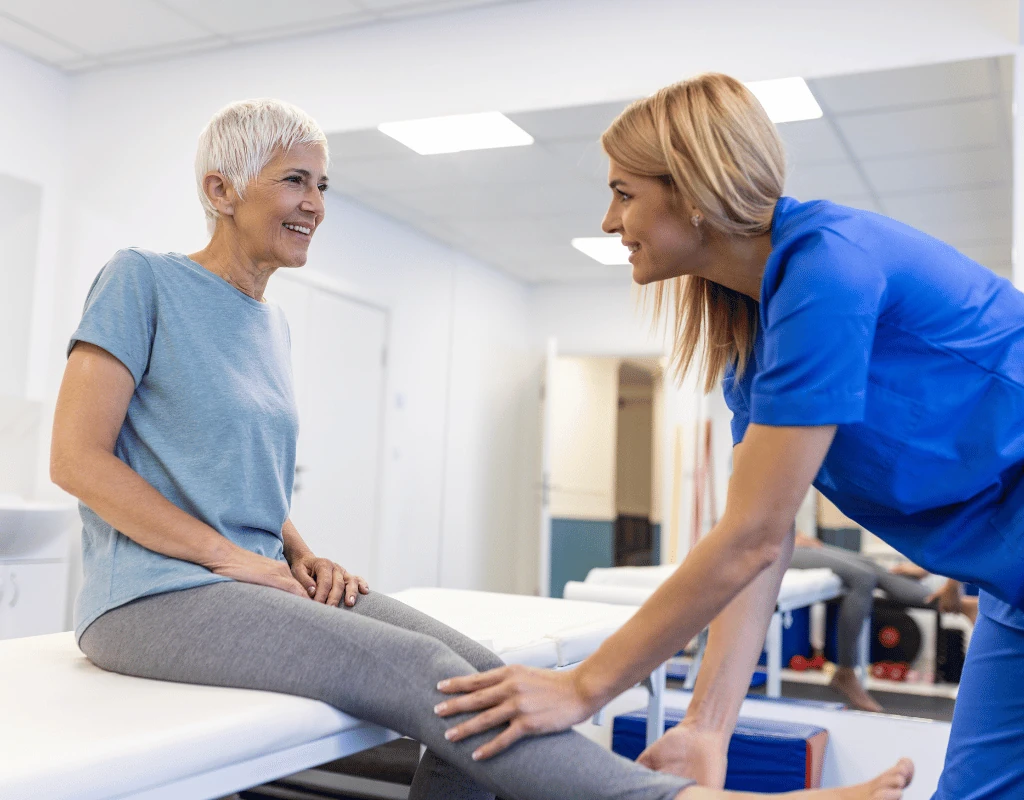 Clinician examining a smiling older womans knee and lower leg on a treatment table