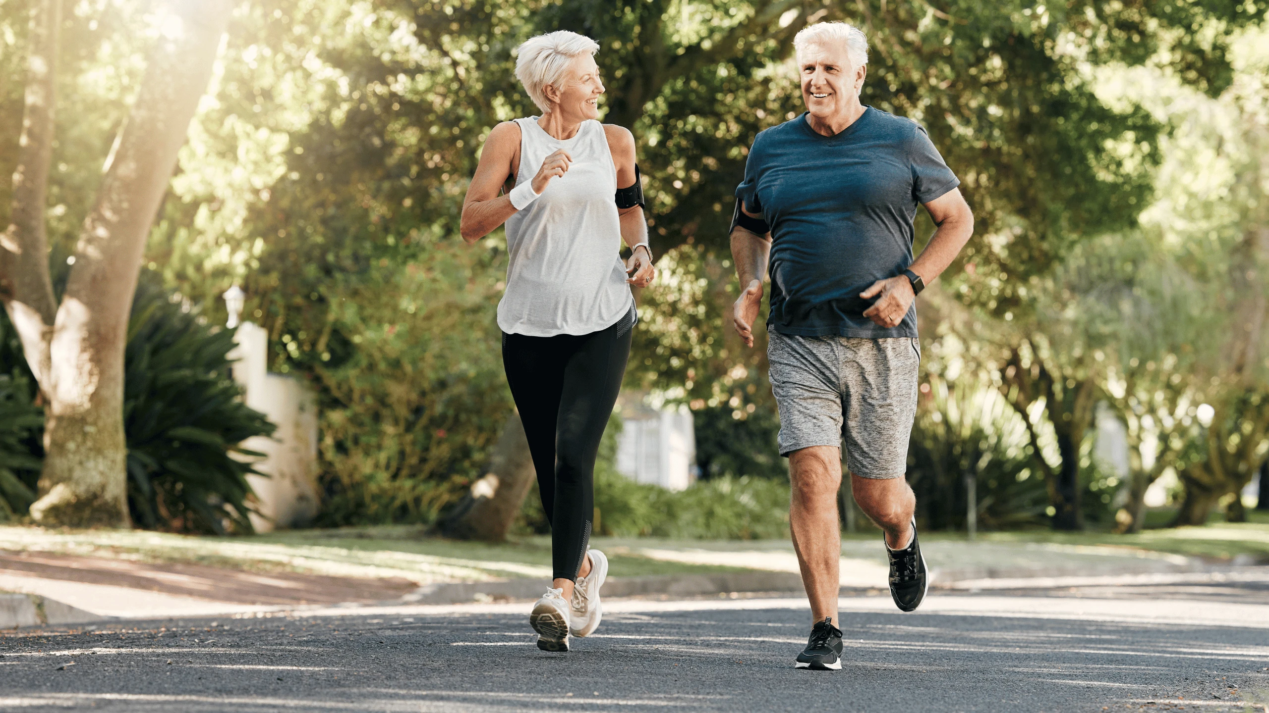 Older man and woman jogging side by side along a tree-lined road