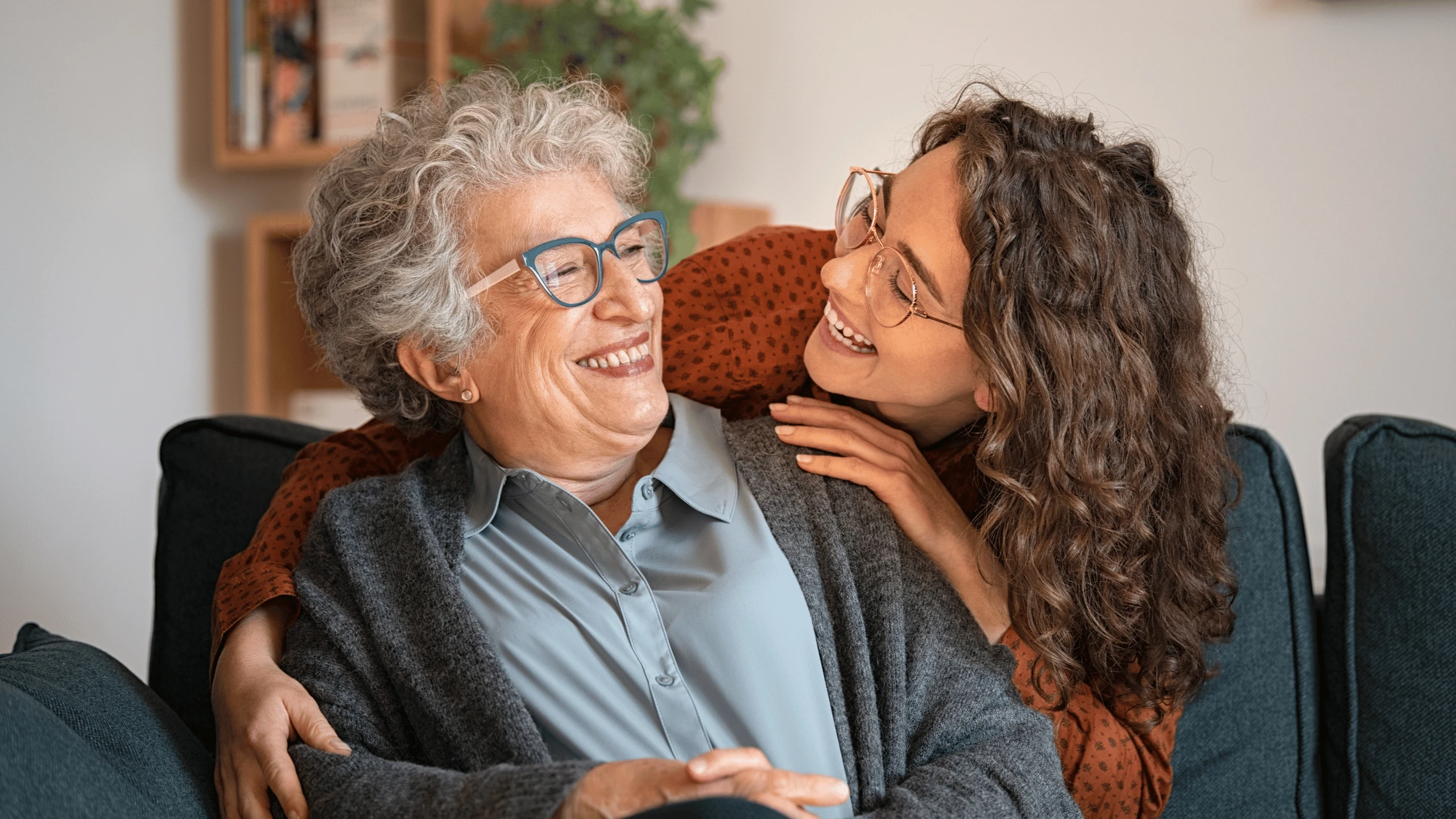 Younger woman leaning in to hug a smiling older woman wearing glasses