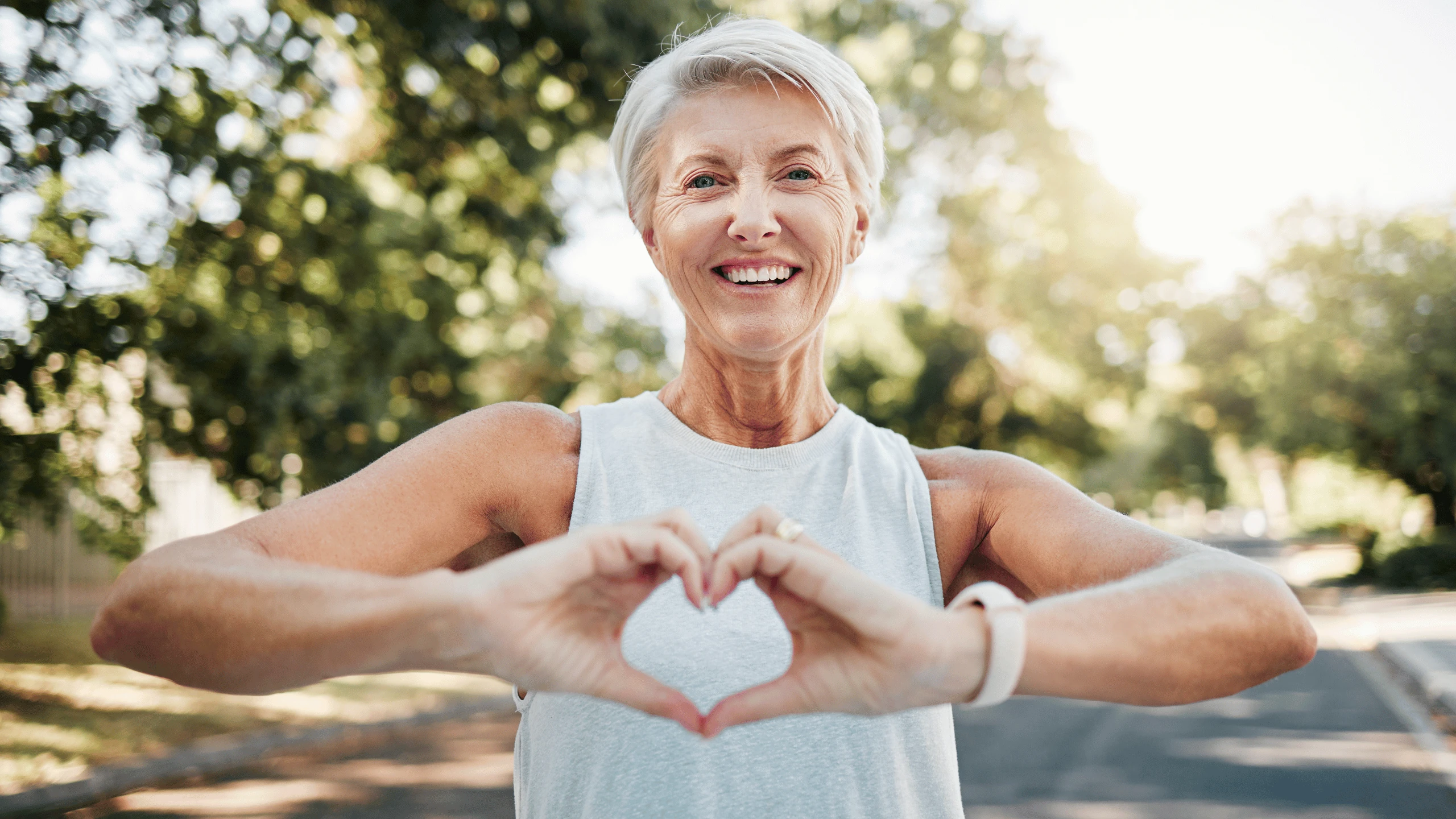 Smiling older woman forming a heart shape with both hands while standing outdoors