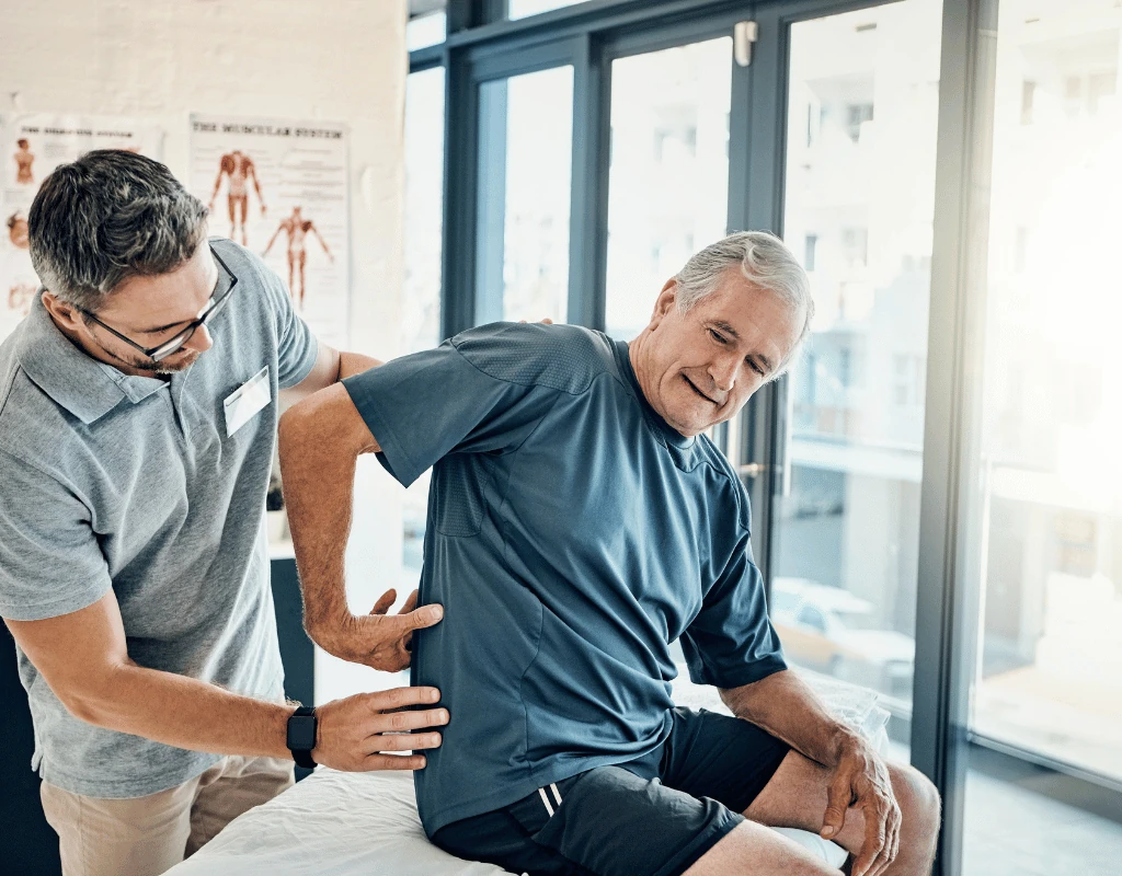 Therapist palpating an older mans lower back while he sits at the edge of a treatment table