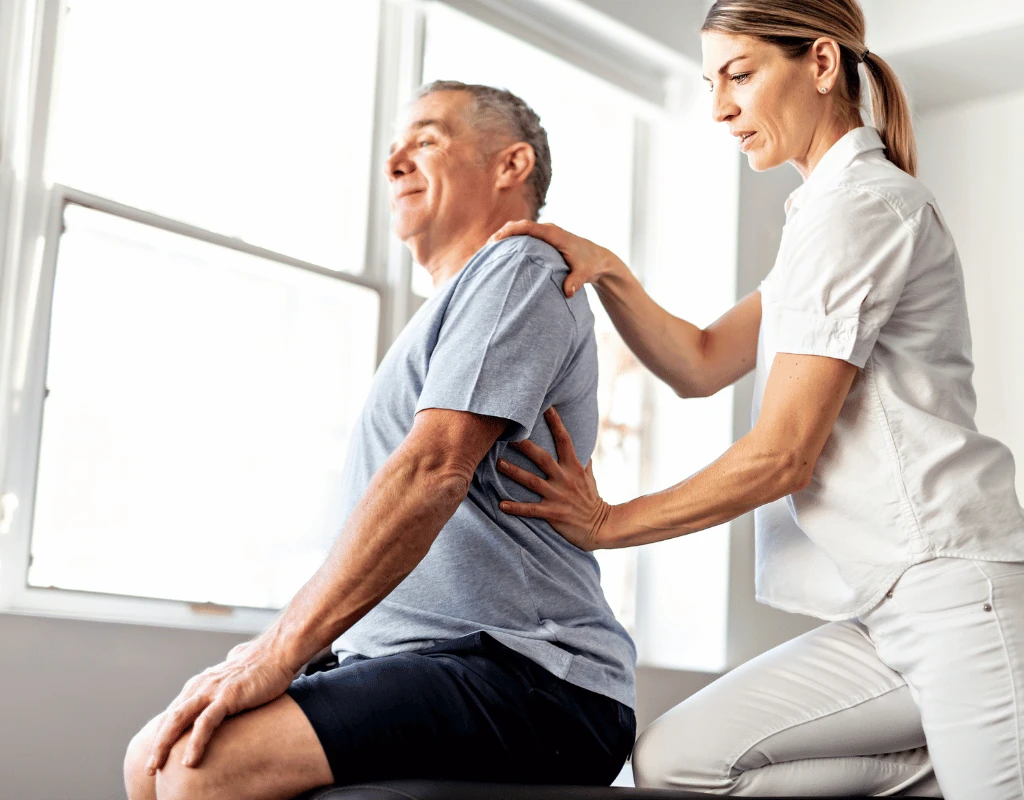 Therapist placing both hands on a seated mans shoulder and upper back