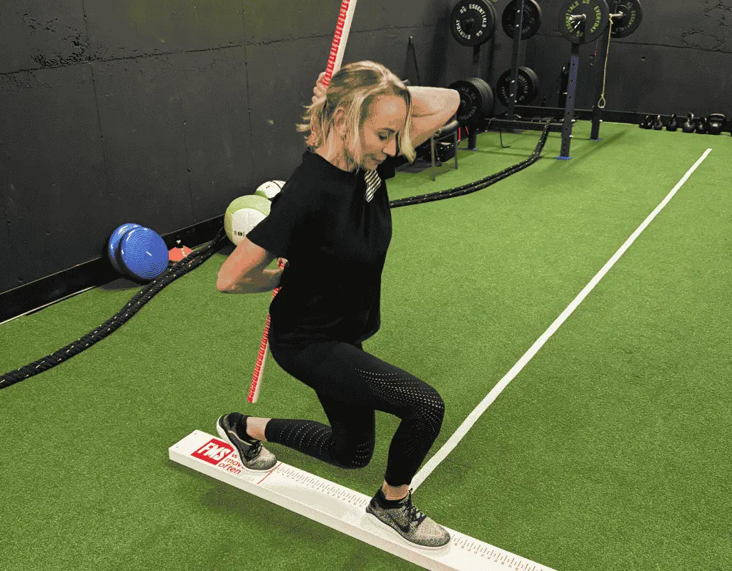 Woman performing an in-line lunge on a narrow board with a dowel held vertically against her back