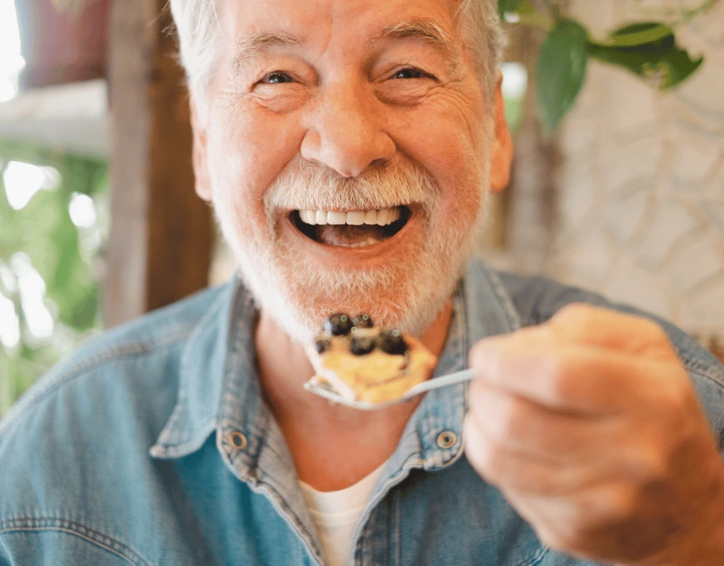 Smiling older man lifting a spoonful of cereal and blueberries towards his mouth