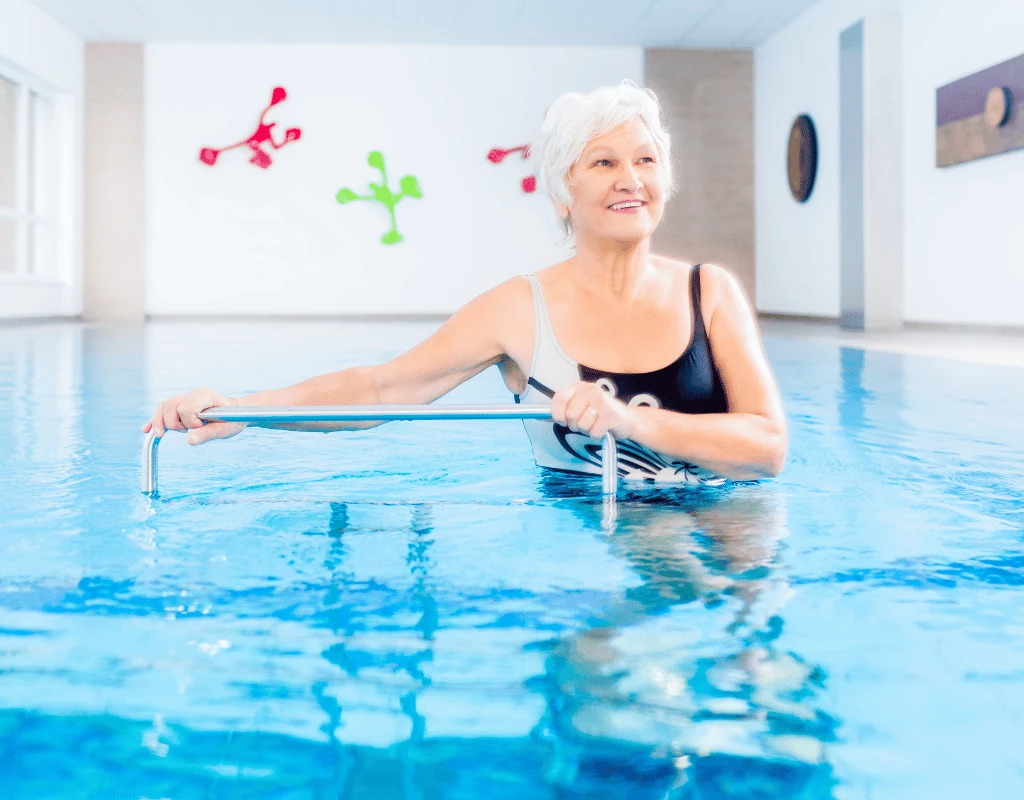 Older woman standing chest-deep in a therapy pool stretching a resistance band between both hands