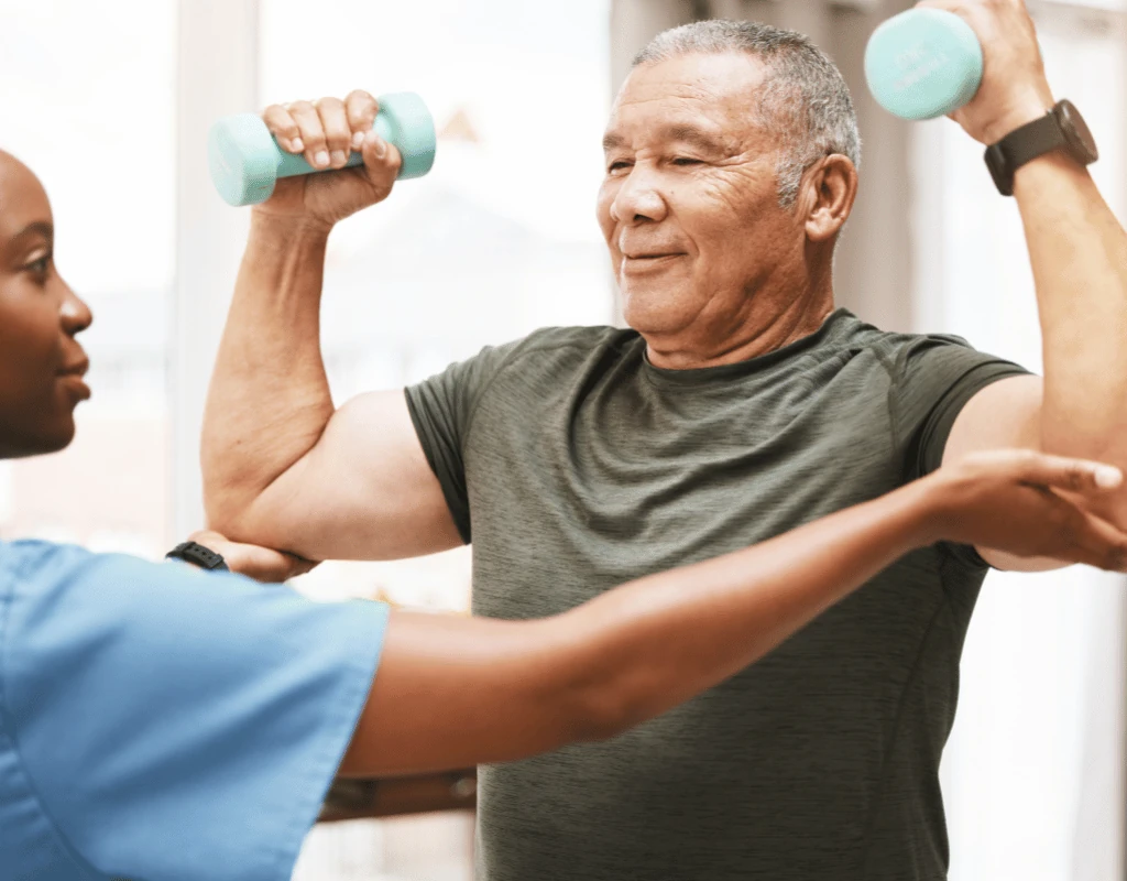 Older man lifting light dumbbells out to the sides while a therapist supports one arm