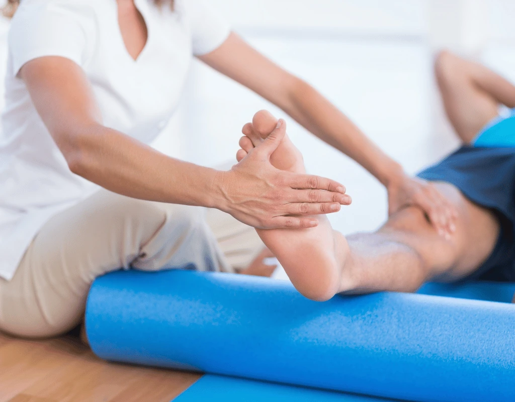 Therapists hands stretching a patients foot and toes with the leg resting on a blue foam roller