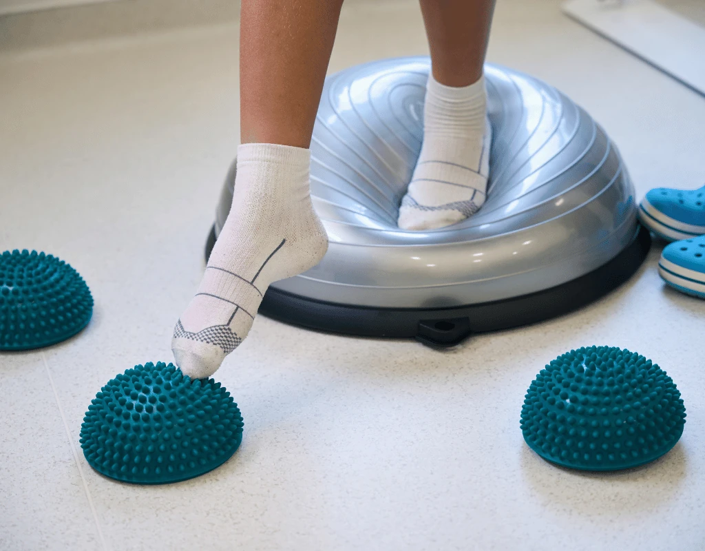 Close view of feet balancing on a domed stability trainer with spiked balance pods on the floor nearby