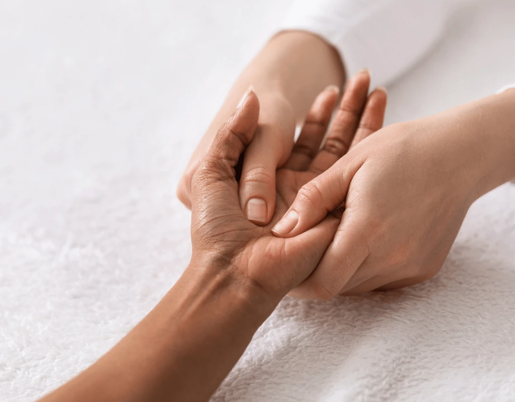Therapists hands working through a patients palm and fingers on a white towel