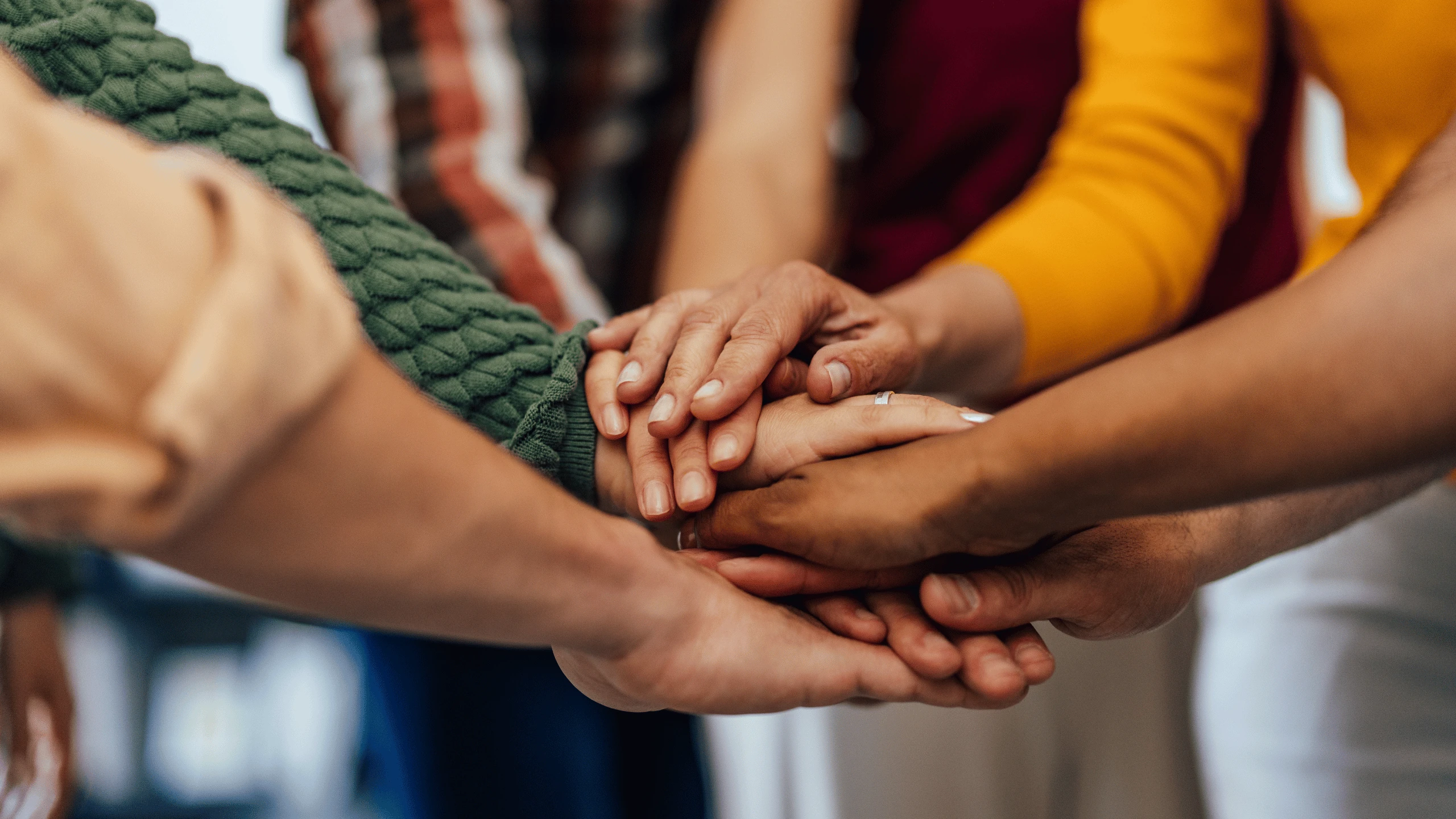 Several hands of different ages stacked together in a circle, one holding a green rope