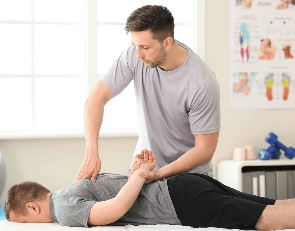 Therapist extending a mans arm out to the side while he lies face down on a treatment table