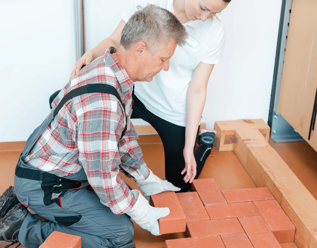 Worker in a back-support harness lifting bricks while a therapist coaches his technique