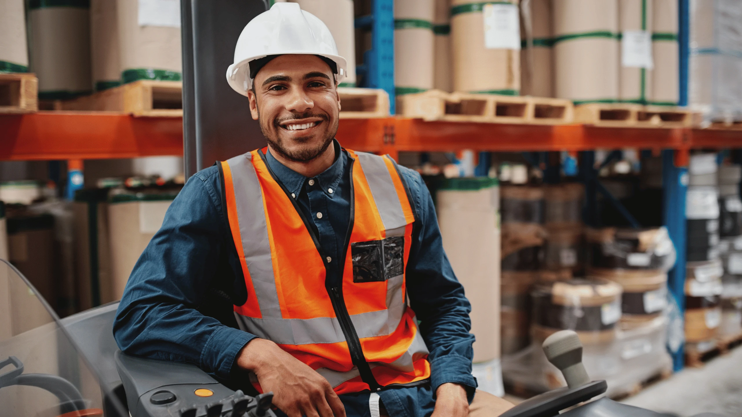 Worker in a hard hat and high-visibility vest seated on a forklift in a warehouse