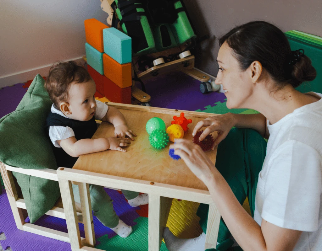 Therapist working with a toddler at a small table covered with colourful toys in a pediatric room