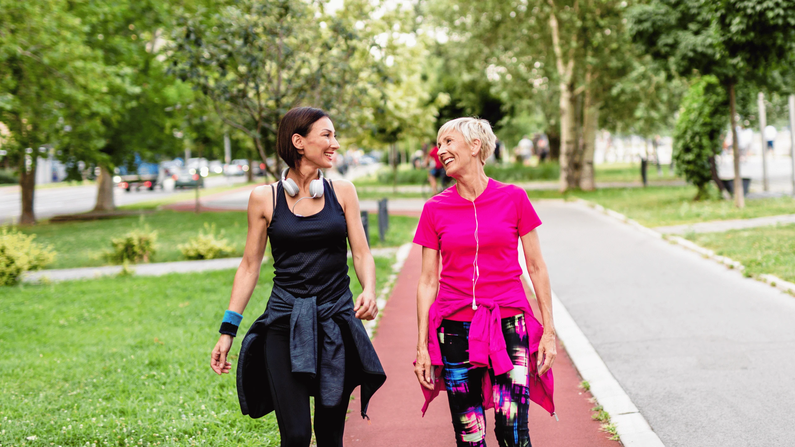 Two women walking along a park path, one pushing a stroller