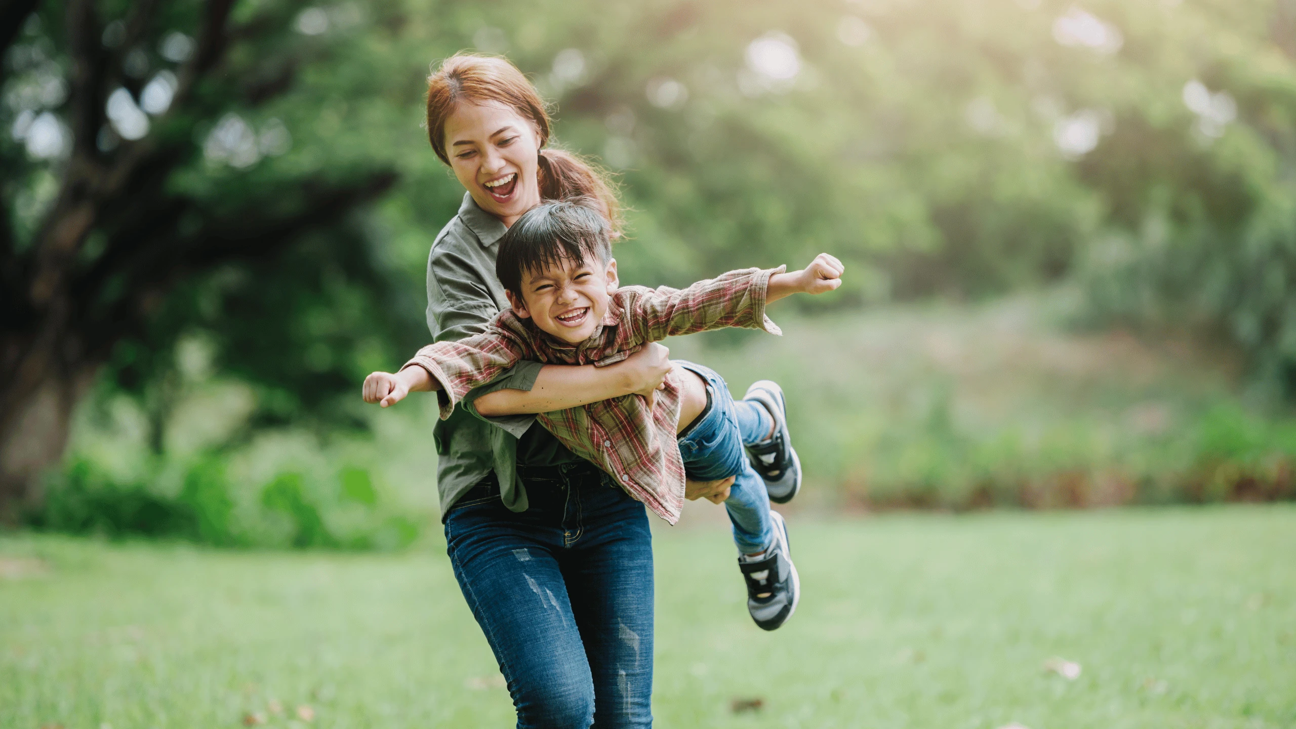 Woman swinging a laughing child through the air on a grassy field