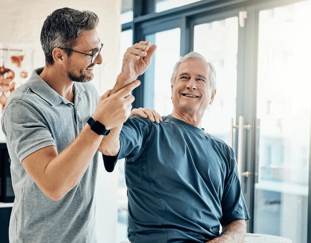 Therapist examining an older mans hand and fingers while he sits in a clinic room