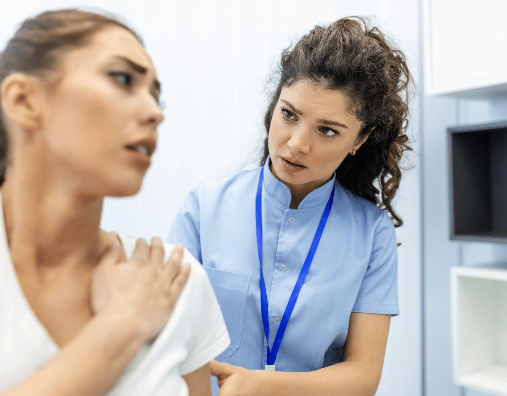 Clinician examining a womans shoulder and upper back from behind in a clinic room