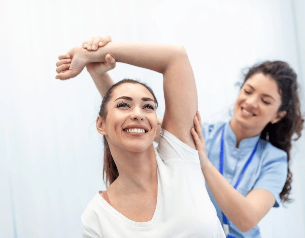 Therapist guiding a smiling womans arm into an overhead stretch across her head