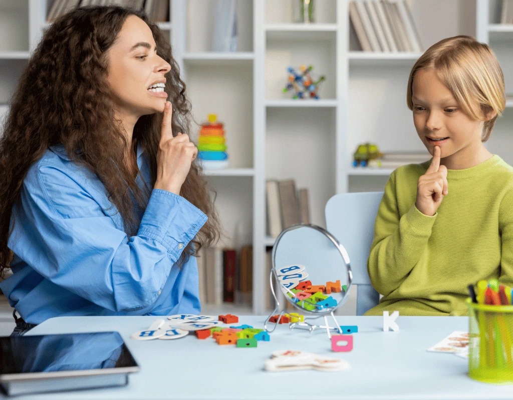 Speech therapist working with a child at a table covered in learning toys and articulation cards