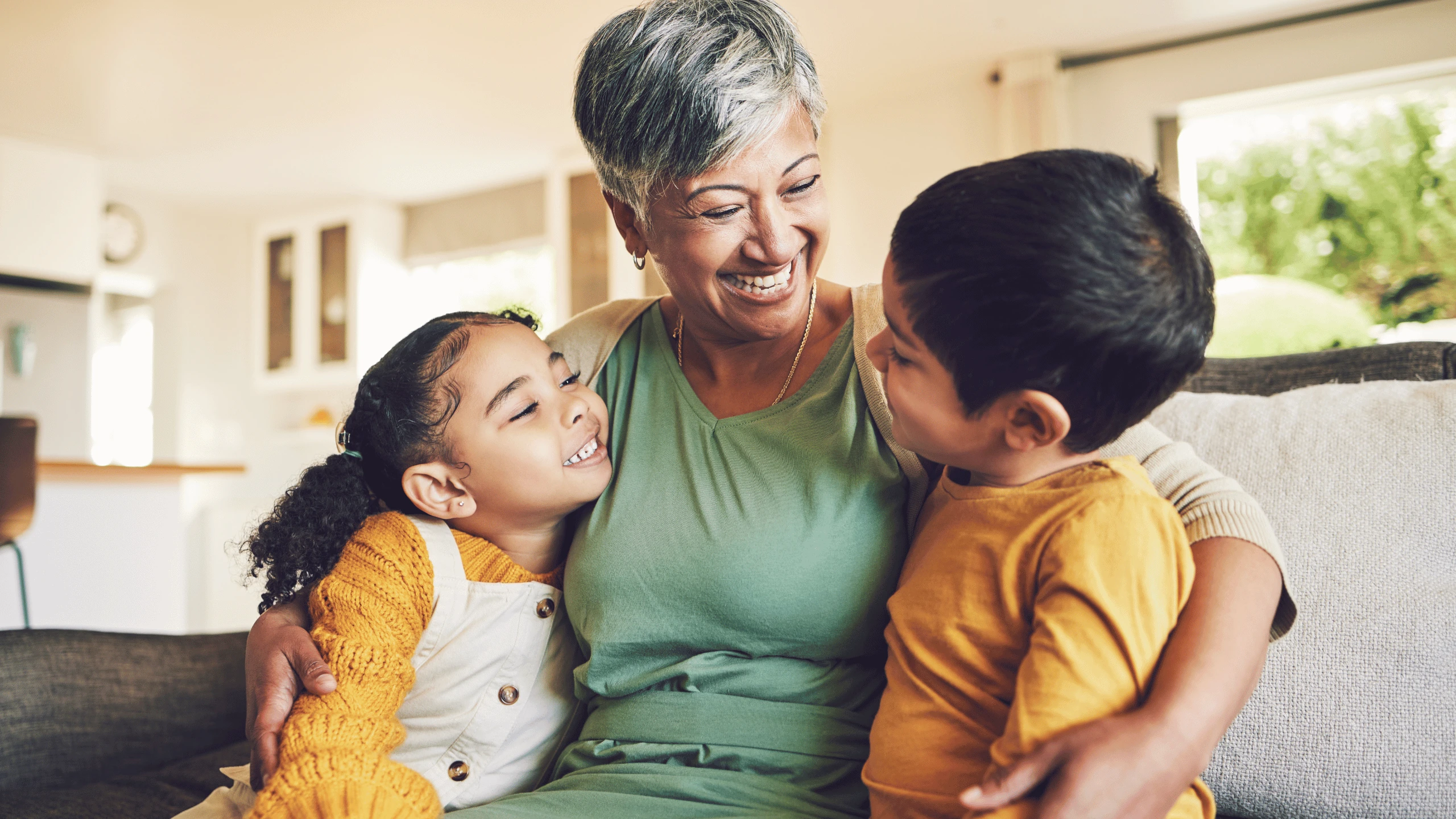 Older woman laughing on a couch with two young children leaning against her