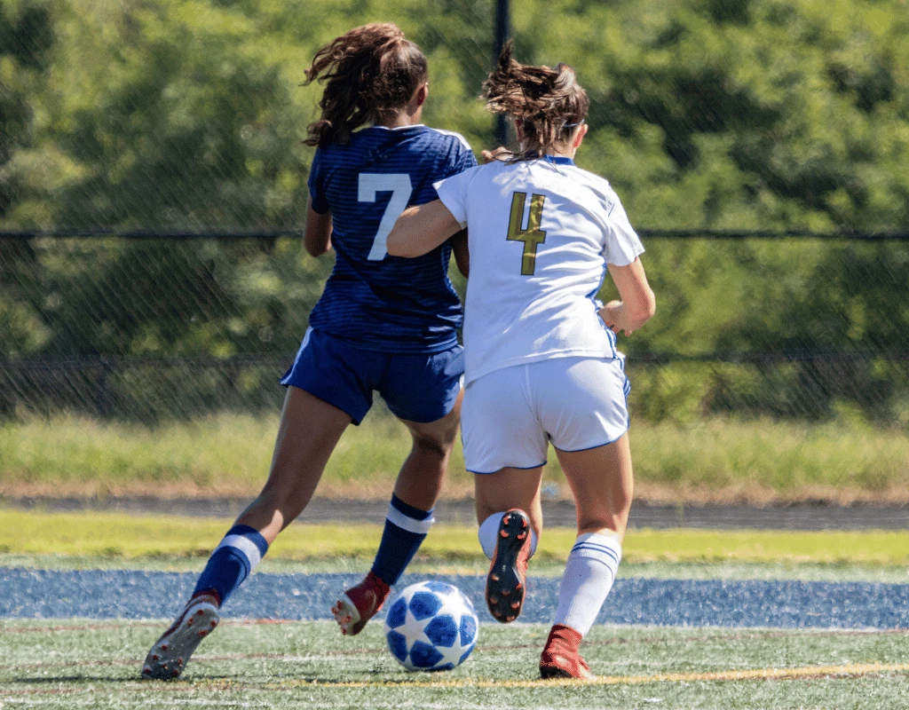 Two girls in soccer kit challenging each other for the ball on a grass pitch