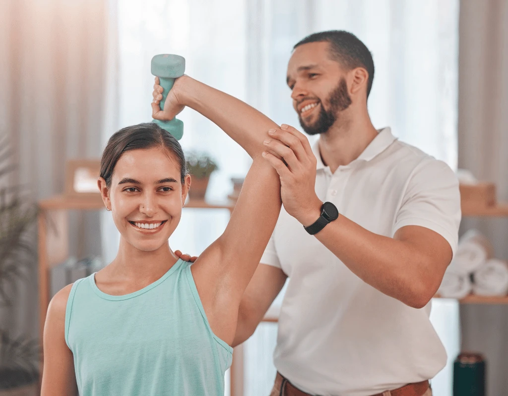 Therapist supporting a smiling womans arm as she lifts a dumbbell overhead