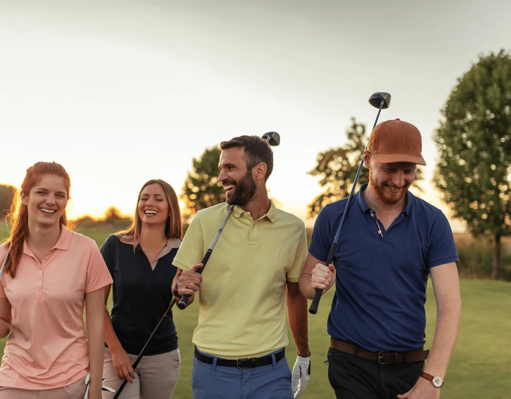 Four adults walking across a golf course carrying clubs at sunset