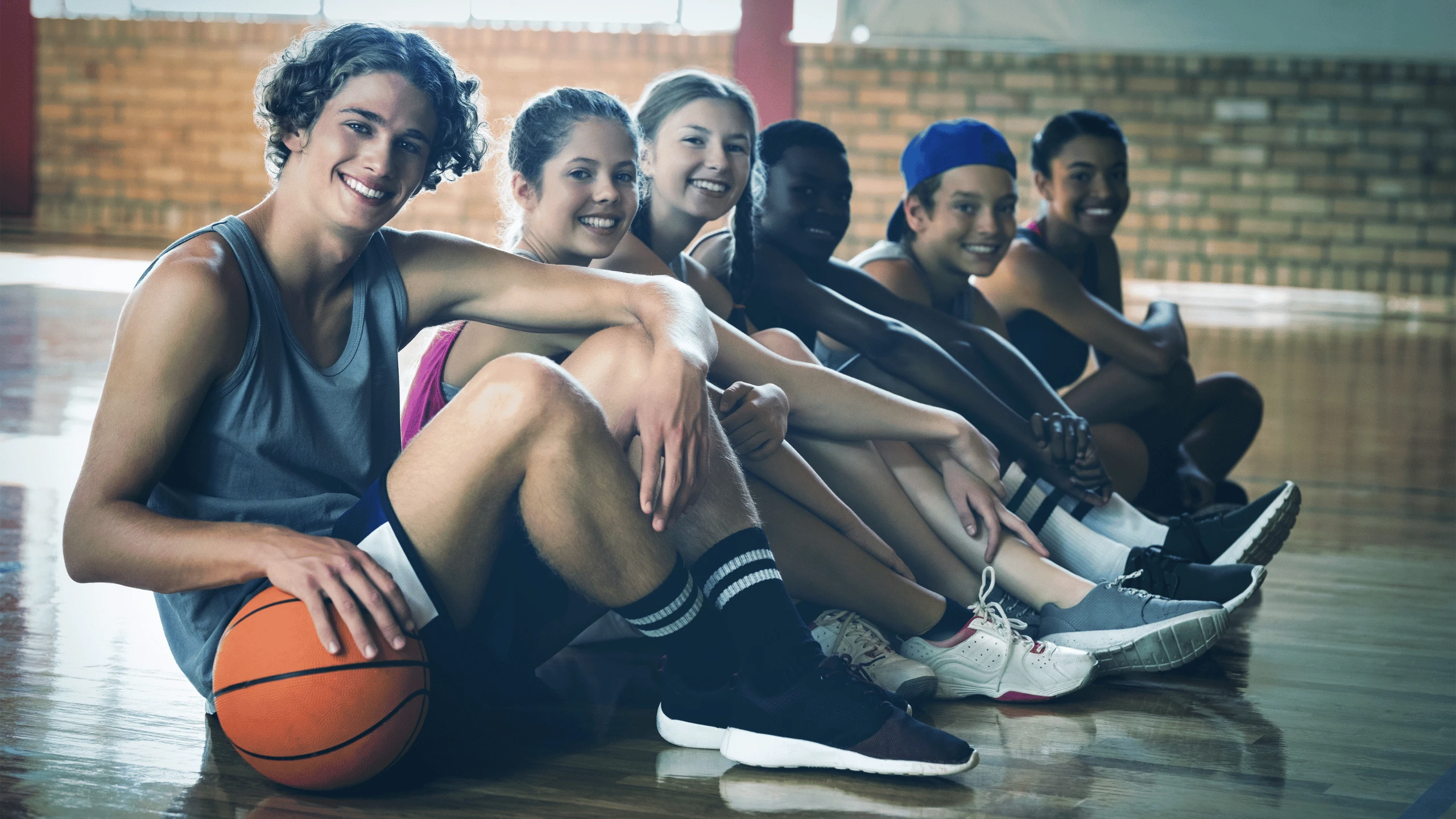 Group of young athletes sitting together on a gym floor with a basketball beside them