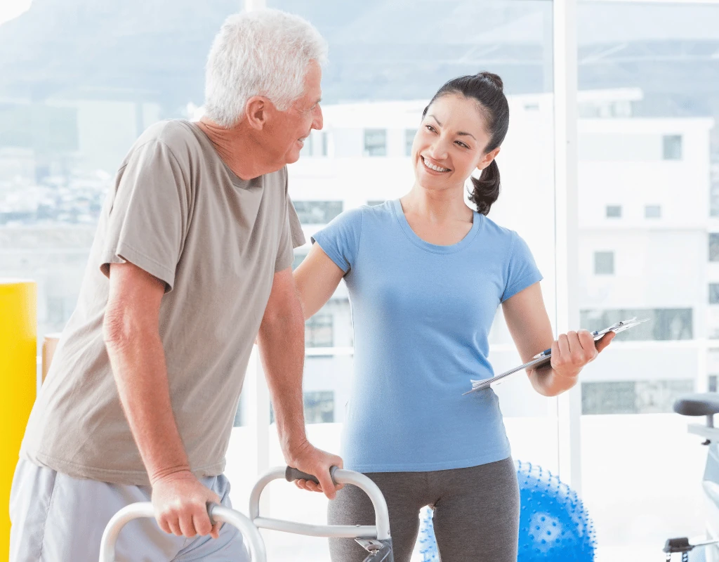 Therapist walking beside an older man as he uses a rolling walker in a therapy room