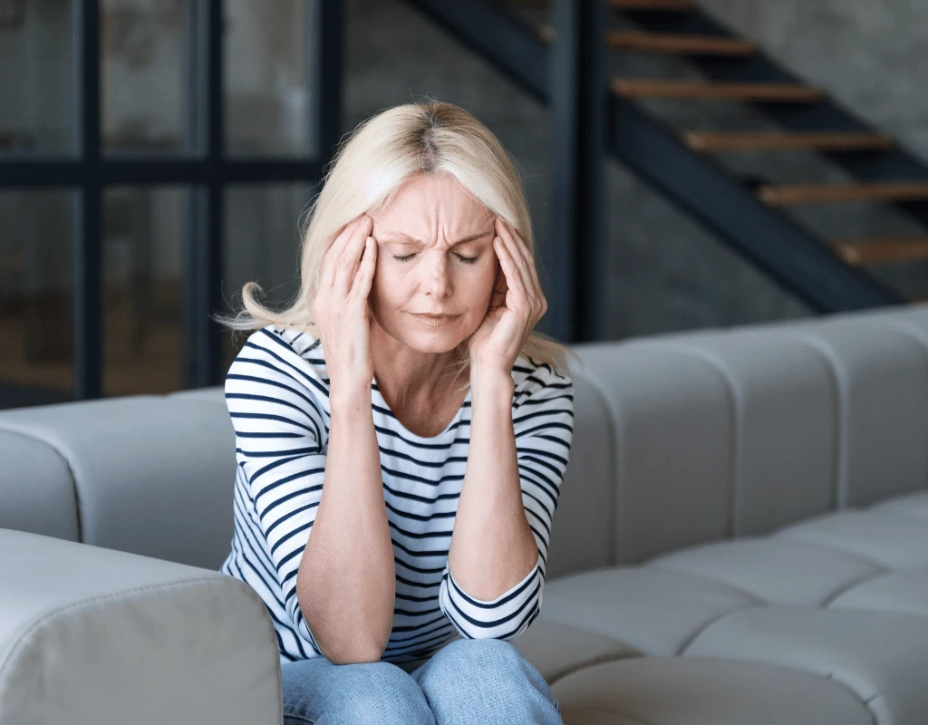 Woman sitting on a sofa holding both hands to her head with her eyes closed