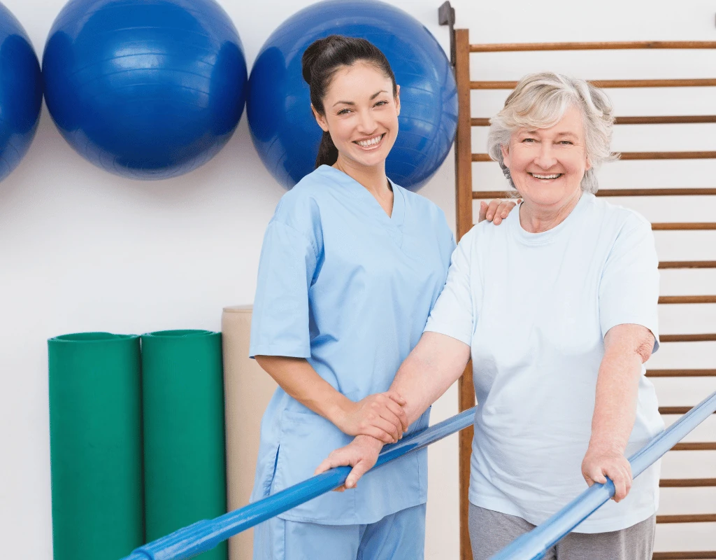 Therapist and an older woman each holding one end of a blue resistance band beside a rack of exercise balls