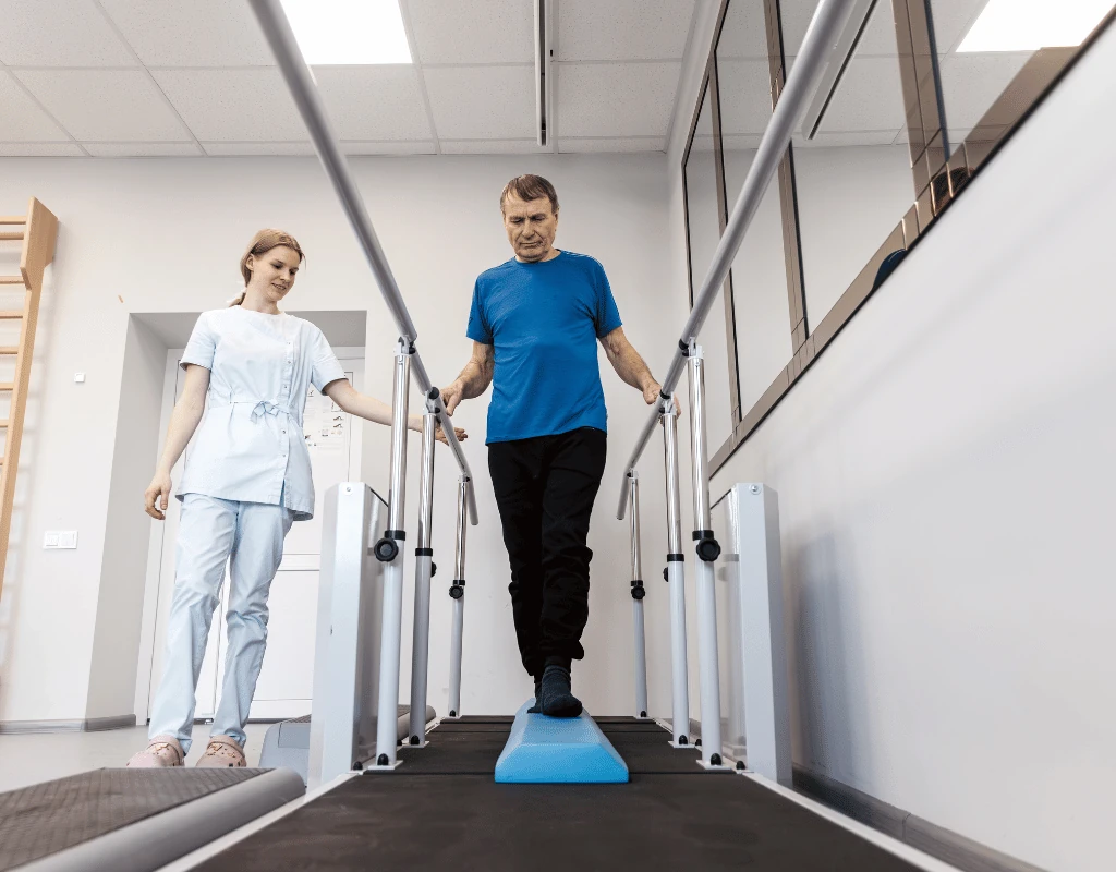 Man walking on a balance pad between parallel bars while a therapist in white watches closely
