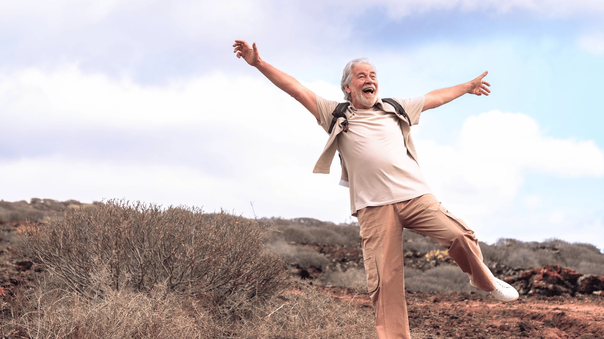 Older man standing on a rocky hillside with both arms outstretched to steady himself