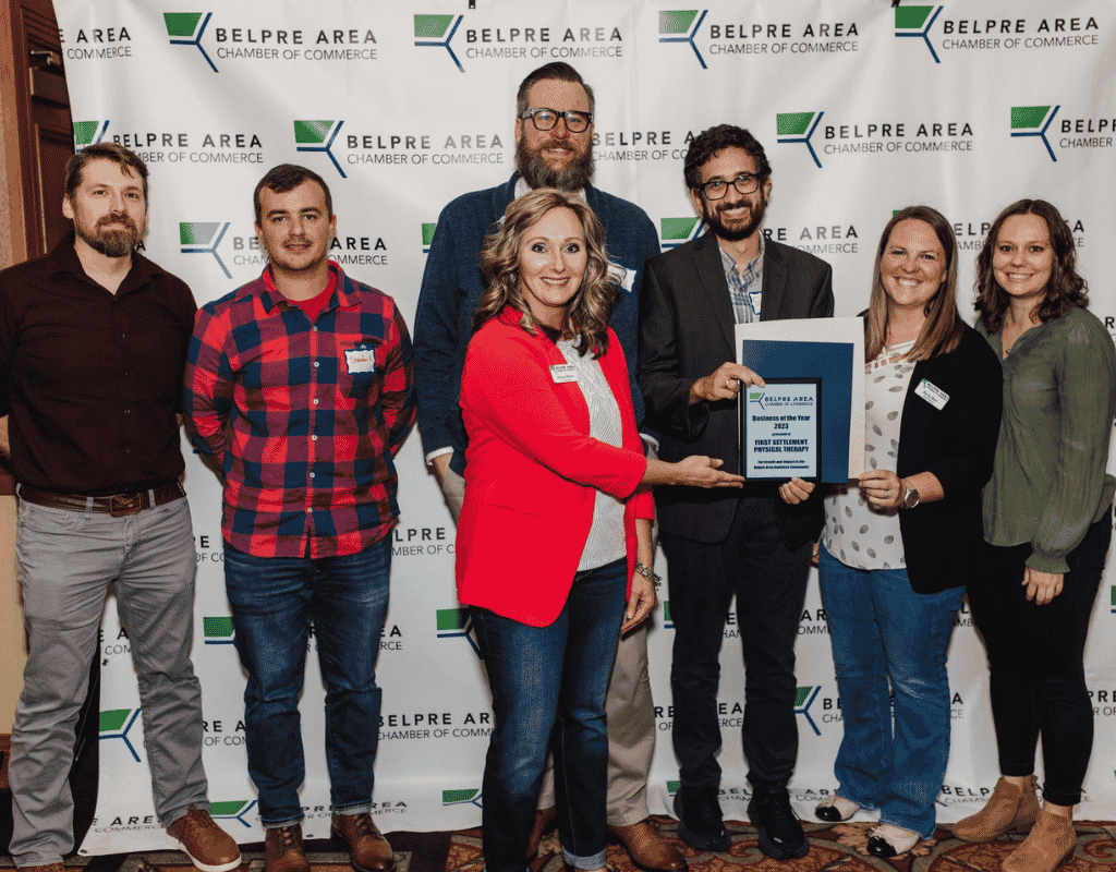 Group of eight people holding a framed award in front of a Belpre Area Chamber of Commerce backdrop