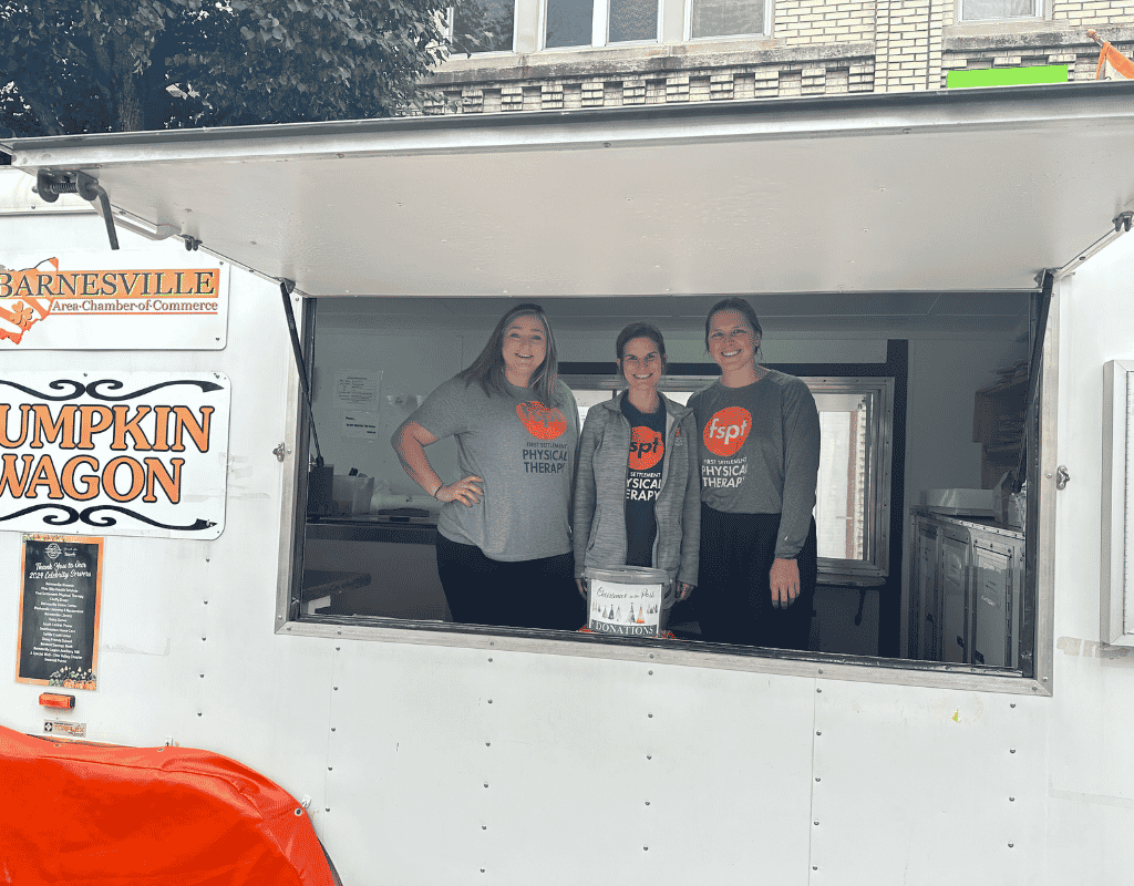 Three staff members in matching shirts standing inside a Barnesville Pumpkin Wagon concession trailer