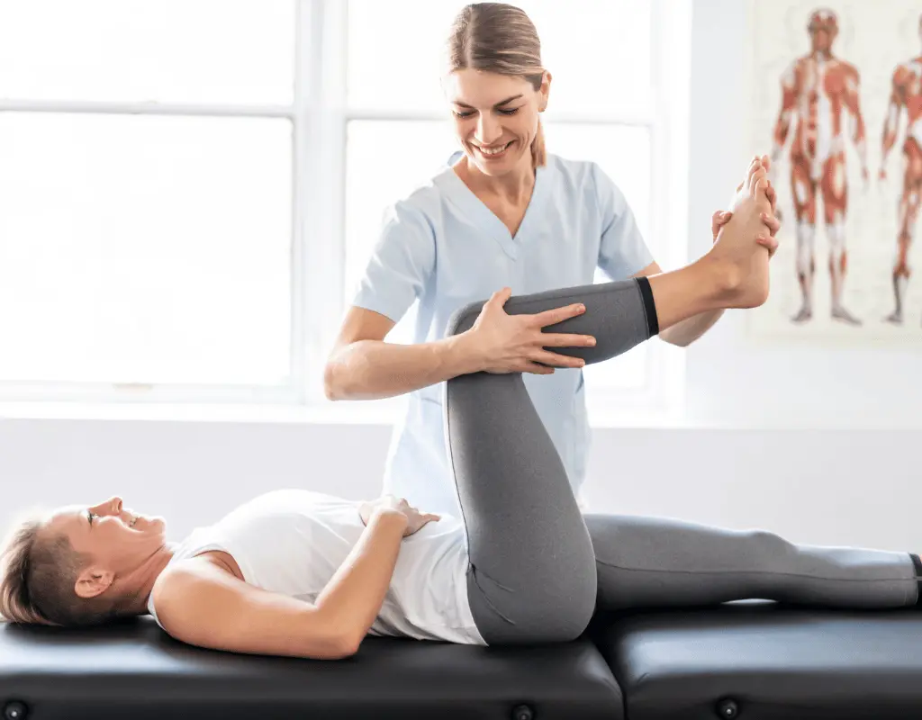 Therapist supporting a womans raised leg in a hamstring stretch while she lies on her back on a treatment table
