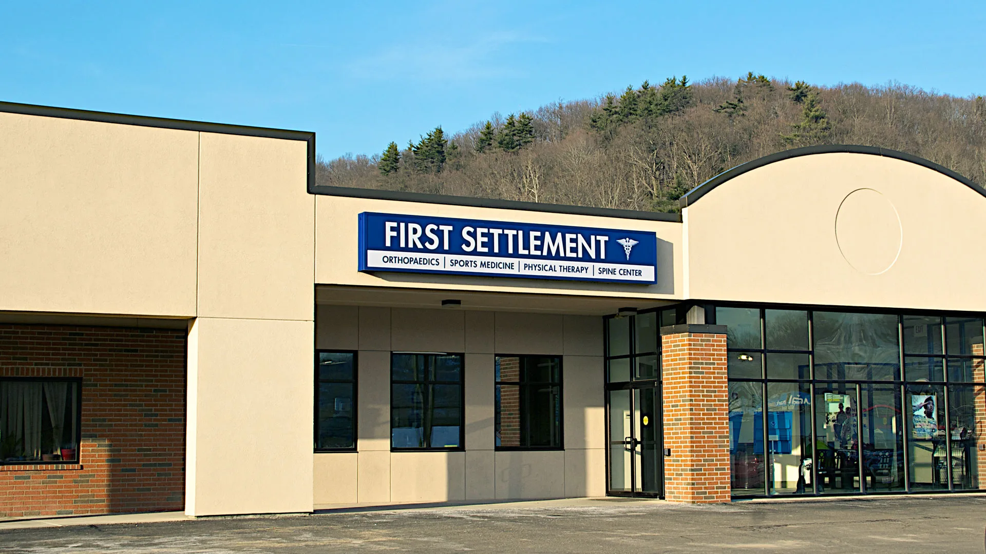 Tan building with a curved architectural entry and a First Settlement sign above the glass doors