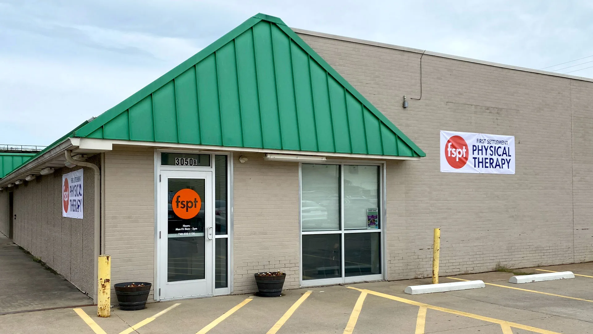 Building with a green metal roof over the entrance and a First Settlement Physical Therapy sign on the wall