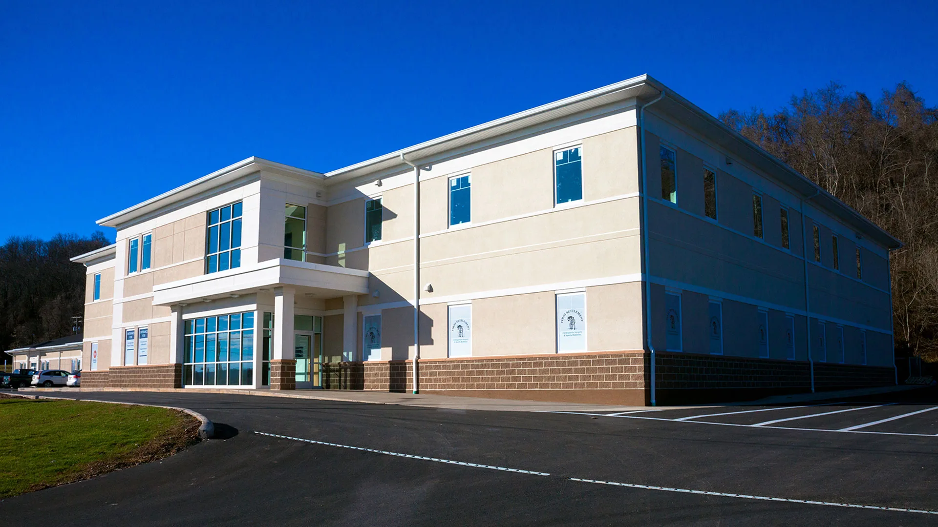 Two-story white and blue medical office building with a paved parking lot alongside