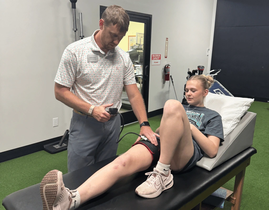 Male therapist using a handheld device to set the pressure on a blood flow restriction cuff around a patient lying on a treatment table