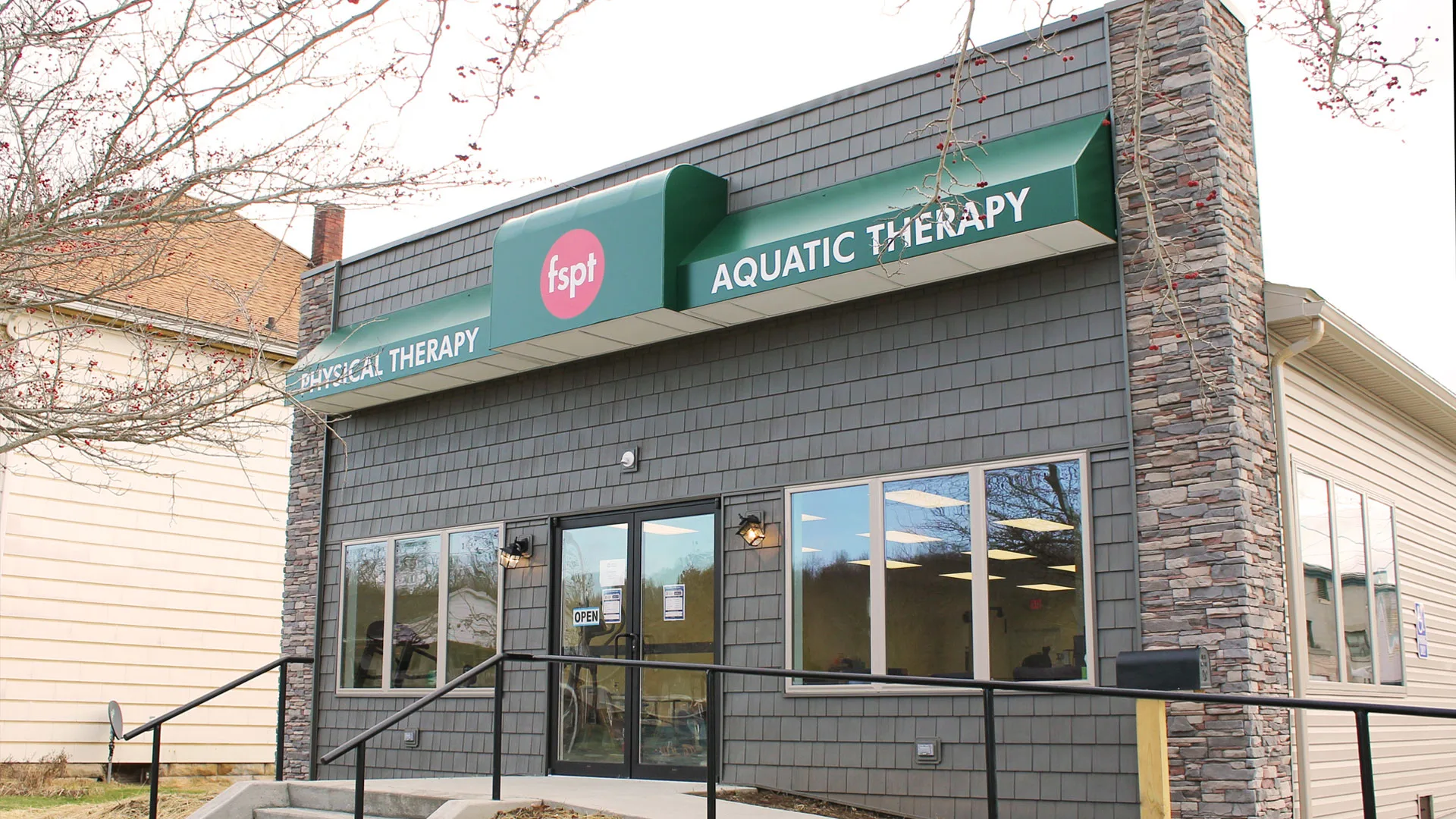 Stone and grey building with green awnings reading Physical Therapy and Aquatic Therapy above the windows