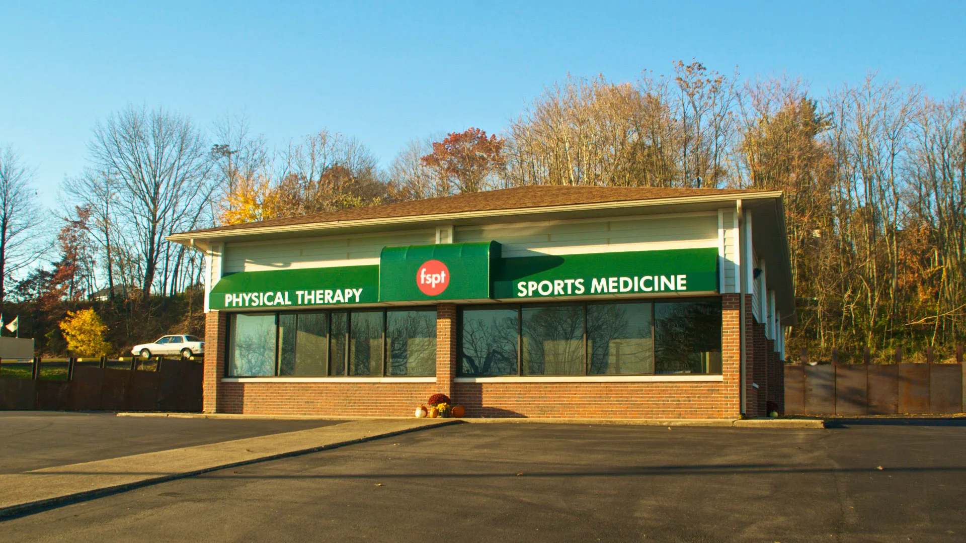 Building with a green awning reading Physical Therapy and Sports Medicine, framed by autumn trees