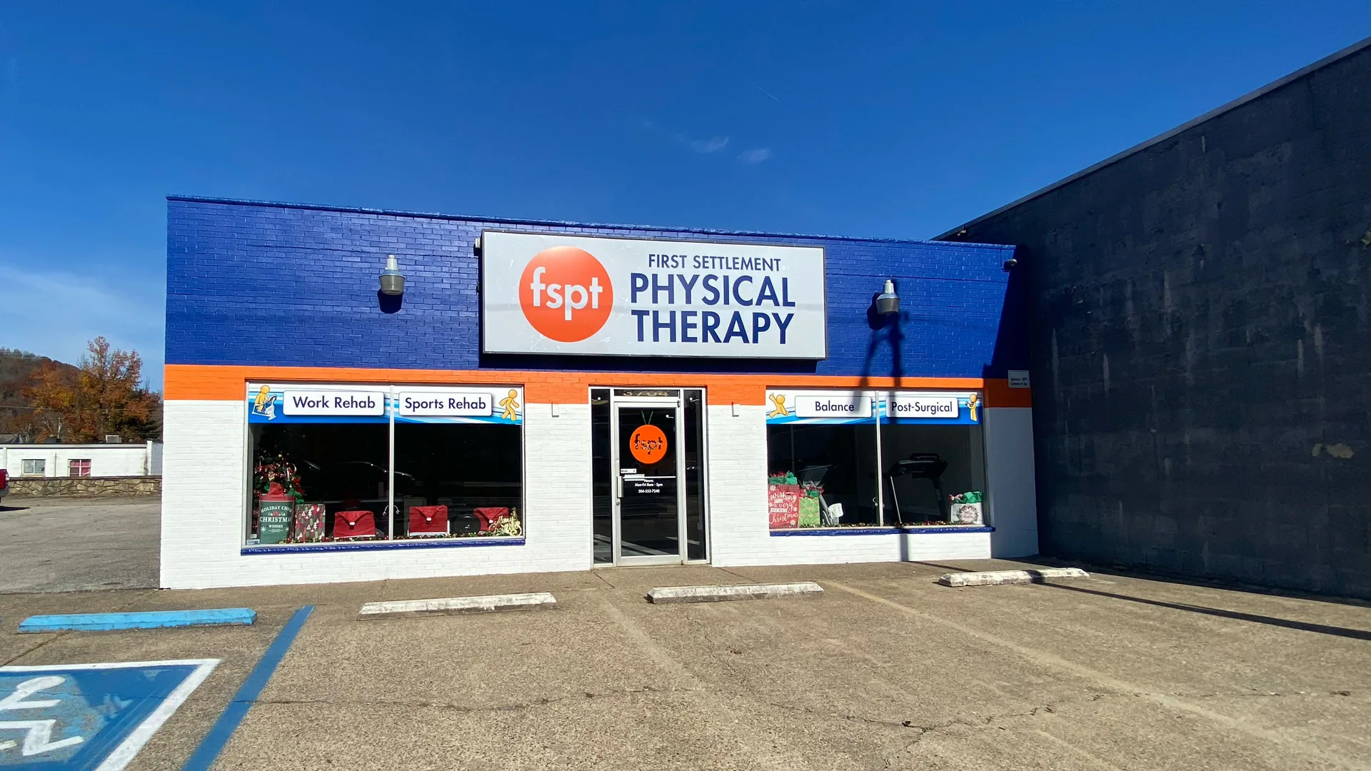 Single-story clinic unit with a large blue First Settlement Physical Therapy sign and accessible parking spaces in front
