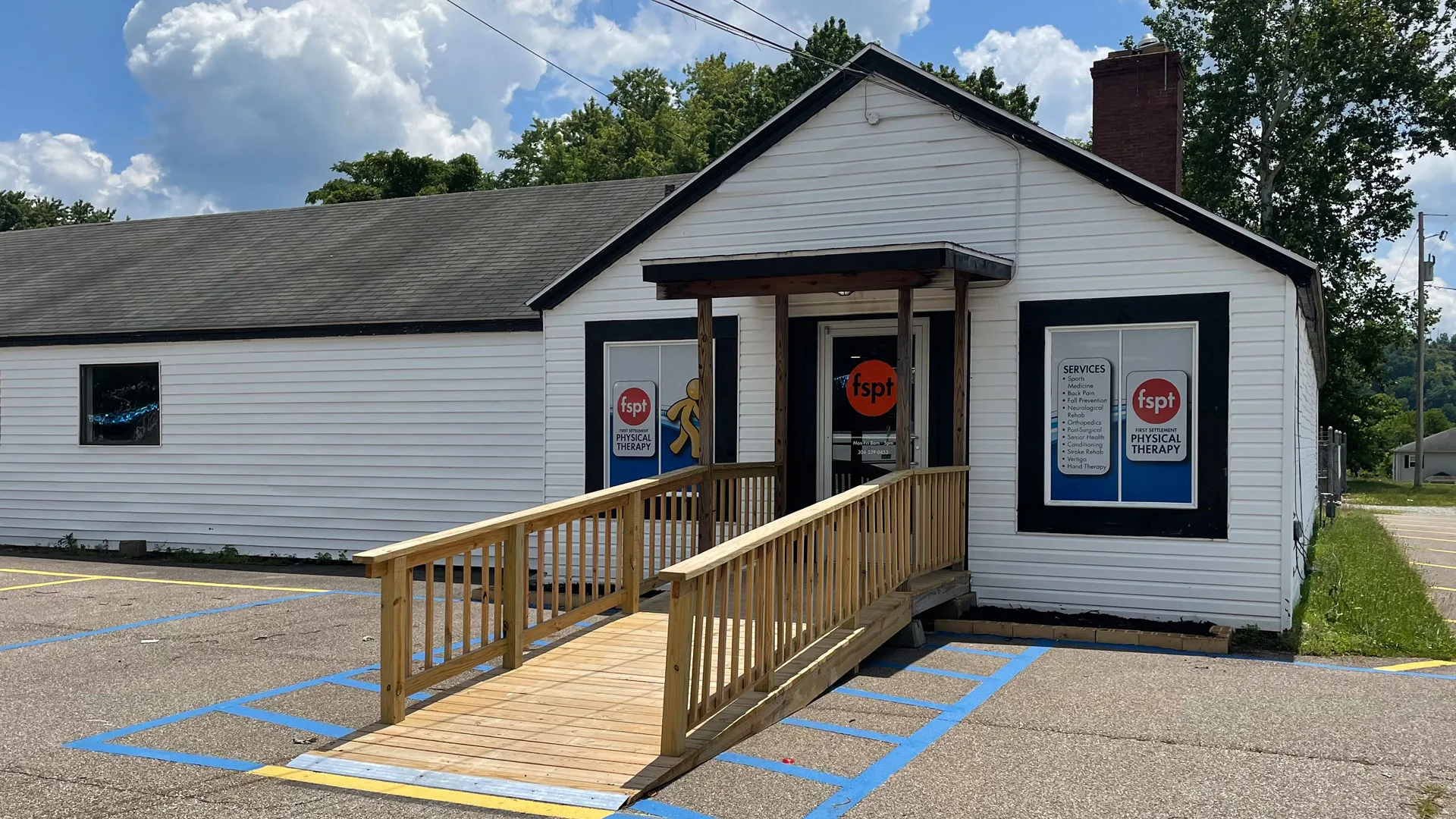 Small white cottage-style clinic with a wooden access ramp leading to the door and marked accessible parking spaces