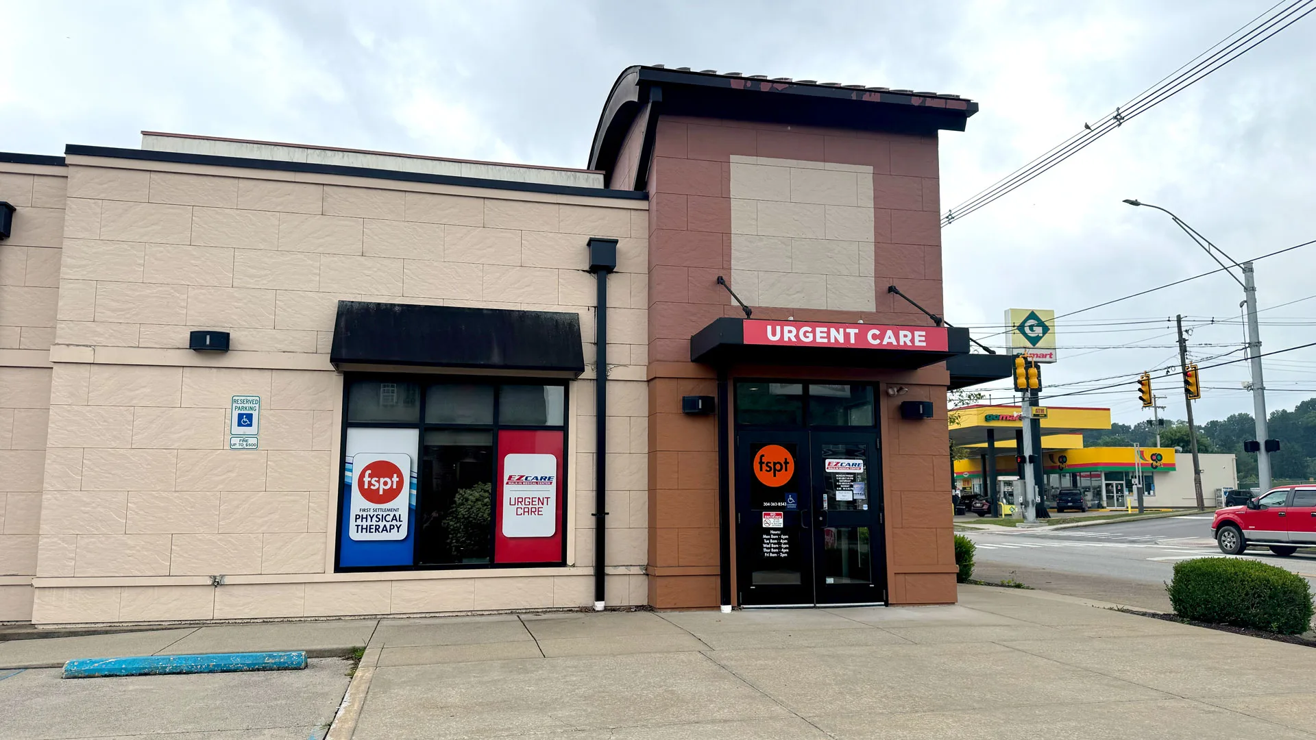 Brick and tan building housing the First Settlement Physical Therapy entrance beside an urgent care, seen from the road