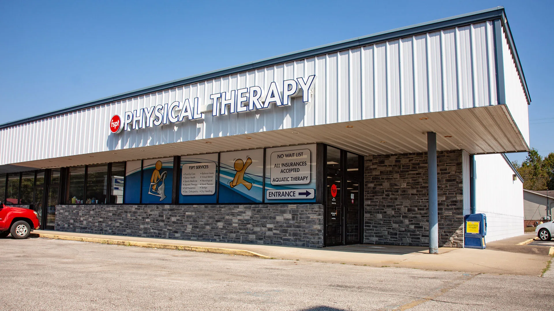 Metal-sided building with a stone base and a Physical Therapy sign above the entrance