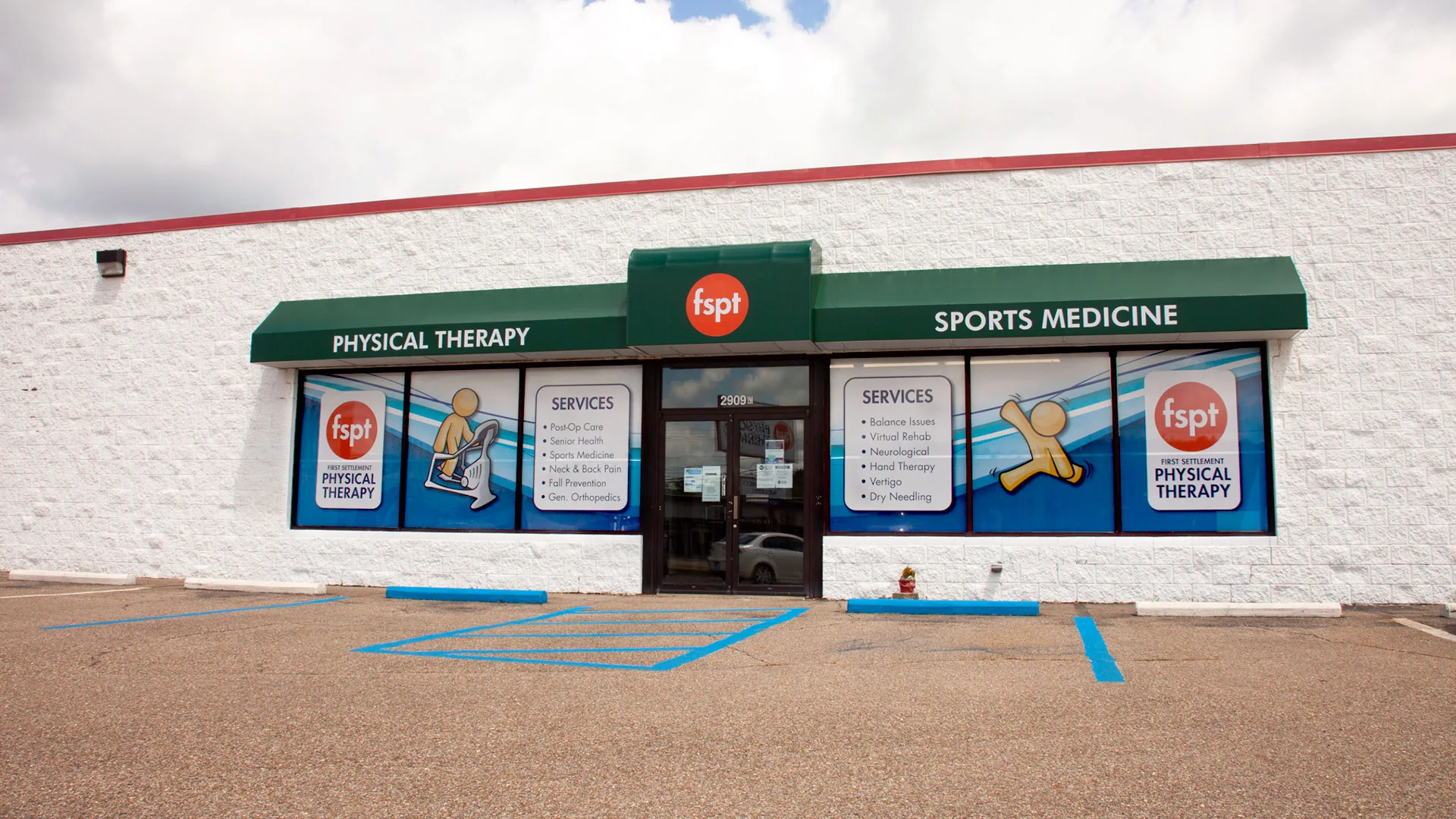 White building with a green awning carrying Physical Therapy and Sports Medicine signage above blue-striped accessible parking